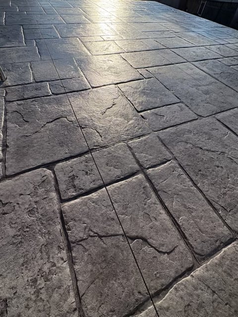 Sunlit gray stone tile patio with geometric pattern and shadows, viewed from above at an angle