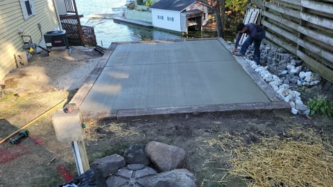 Newly poured concrete pad in backyard with houses and fencing visible in background