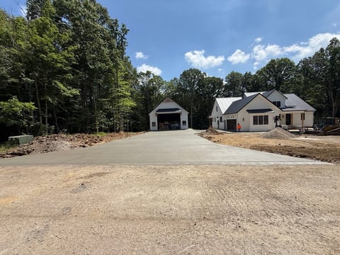 Modern white house with attached garage on gravel driveway surrounded by trees under blue sky