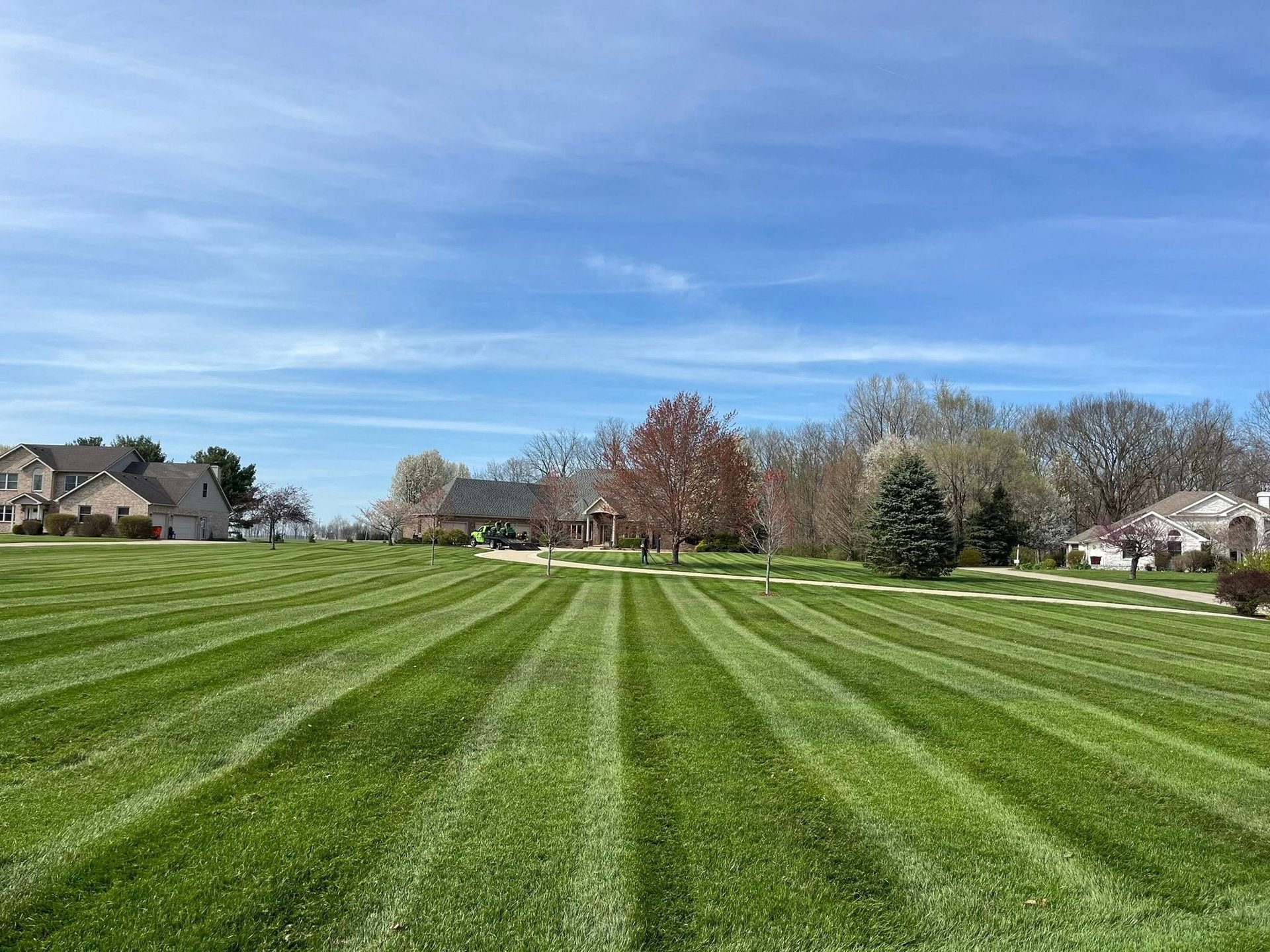 Perfectly striped green lawn extending toward residential houses and bare trees under blue sky