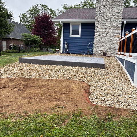 Backyard with gravel patio, concrete pad, and modern house addition with blue siding and stone chimney