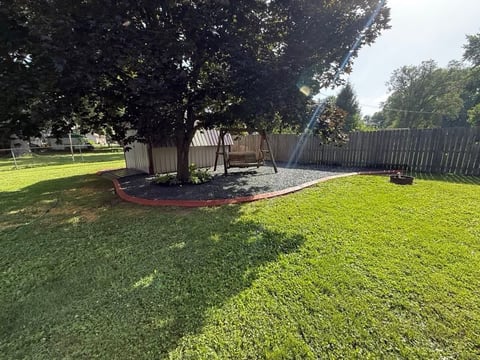 Backyard with mature trees, wooden fence, playset, and green lawn