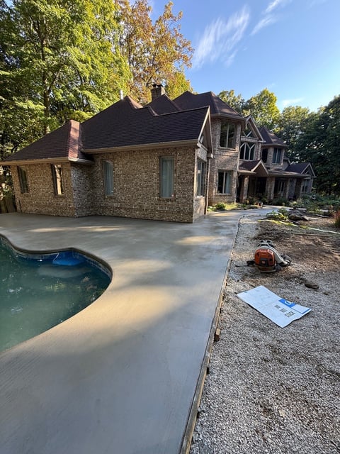 Stone residential home with newly poured concrete patio and swimming pool under construction surrounded by fall foliage