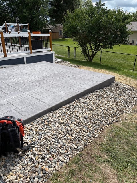 Backyard patio with concrete pavers edged by gravel, featuring a white and wood gate, and fenced yard in background