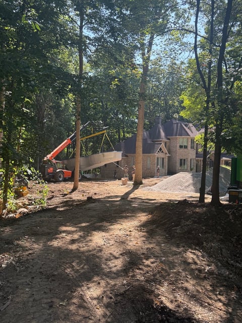 Construction site with orange crane near stone house under construction surrounded by tall trees