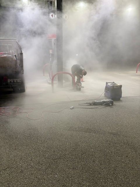 Worker operating pressure washer equipment in thick white steam cloud on wet pavement