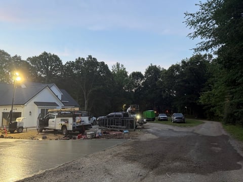 Utility truck and work equipment parked in residential driveway at sunset with trees in background
