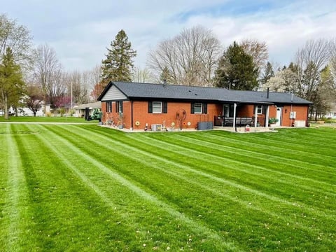 Bright orange brick house with black roof on manicured green lawn with mowed stripes and evergreen trees in background